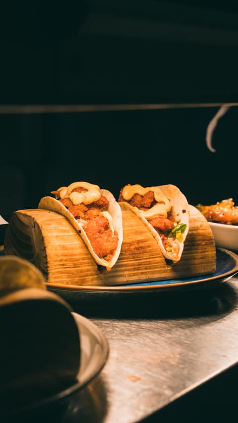 Two crispy-filled tacos with salad and sauce in a wooden taco holder