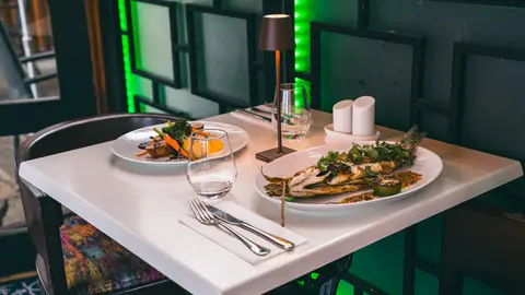 Two evening mains on the table — duck breast and a whole grilled fish — with a glass of water