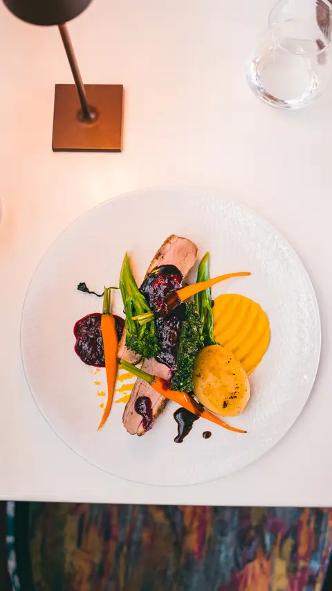 Sliced duck breast with fondant potato, baby carrots and a berry compote, seen from above