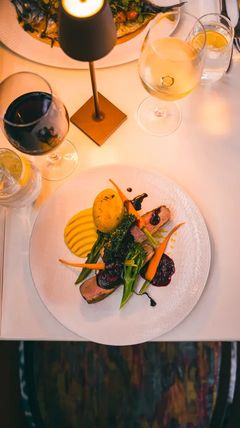 Duck breast with fondant potato and baby carrots, with a glass of red wine, seen from above
