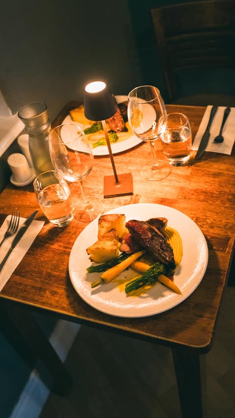Two evening meals and glassware arranged around a glowing table lamp