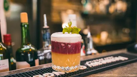 A layered sour cocktail topped with foam and fresh mint on the bar