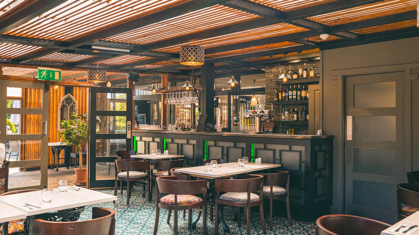 The orangery dining room at Bramley Lodge — timber-slatted ceiling, patterned green tiles and the marble-topped bar