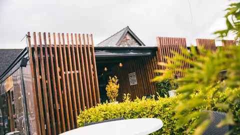 The timber-slatted entrance from the terrace, with a table set among the greenery
