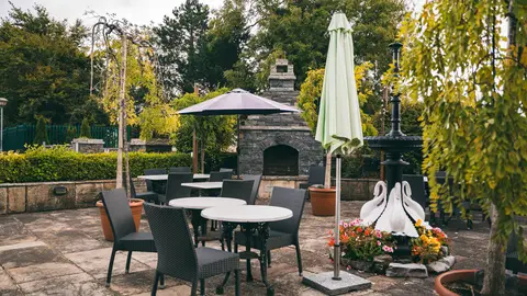The garden terrace — tables under parasols beside the stone fireplace, with the swan planter in bloom