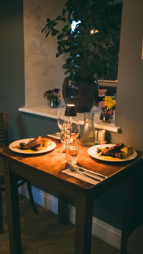 A table for two set with evening mains beneath a leafy plant by the window